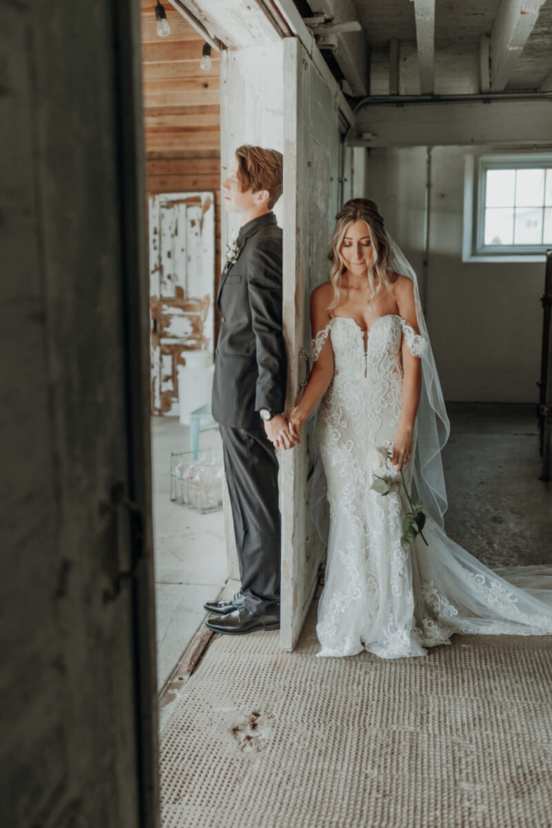 Bride and groom hold hands around a door for first touch before their wedding