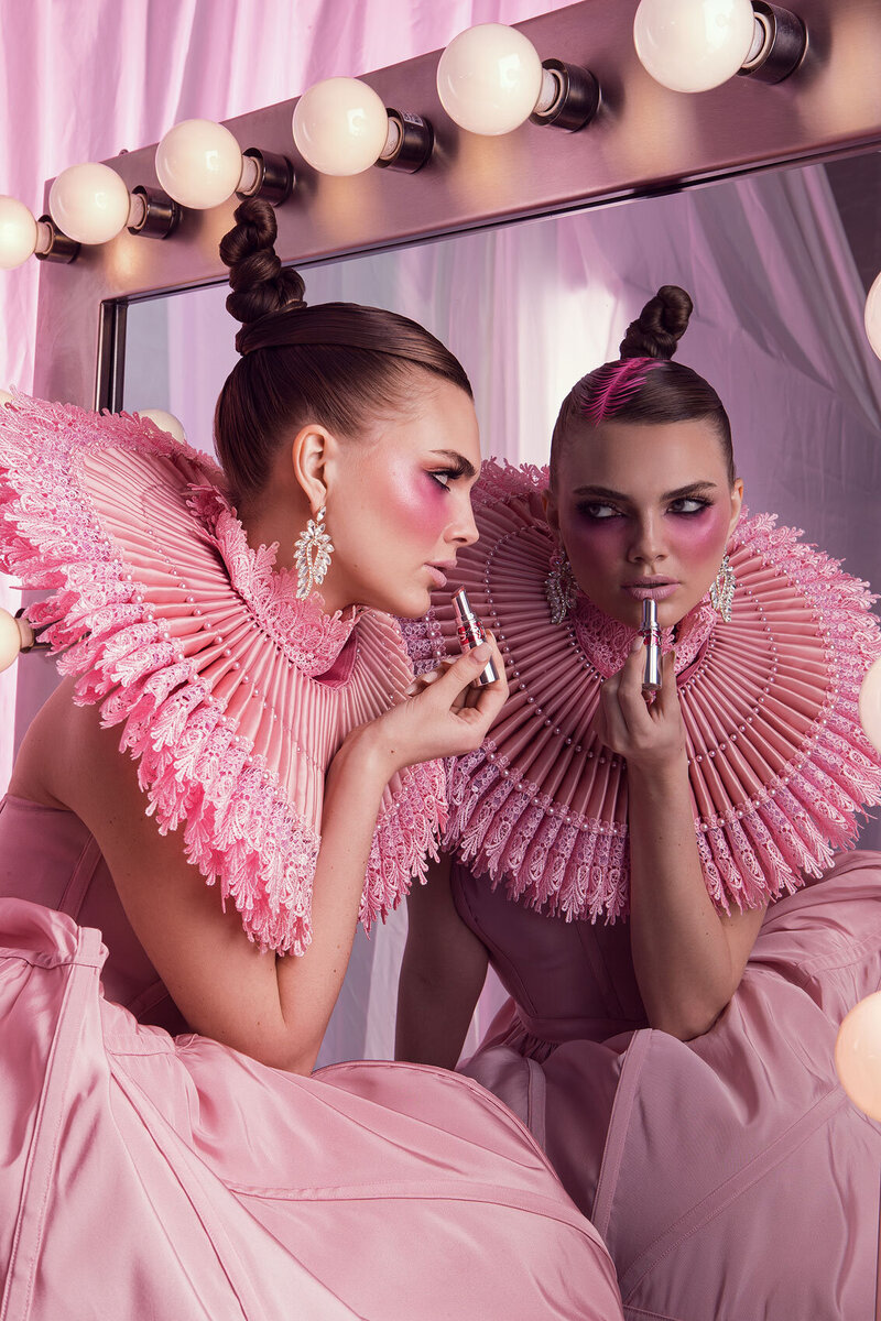 Stylized portrait of Ashley in a pink ruffled outfit, posing alongside a pink-toned mirror, captured by Ylva Erevall.