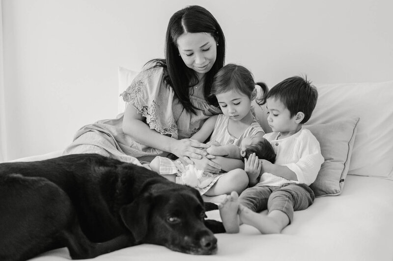 Black and white photo of Mai and her children holding their newborn sitting while their dog sleep by their foot.