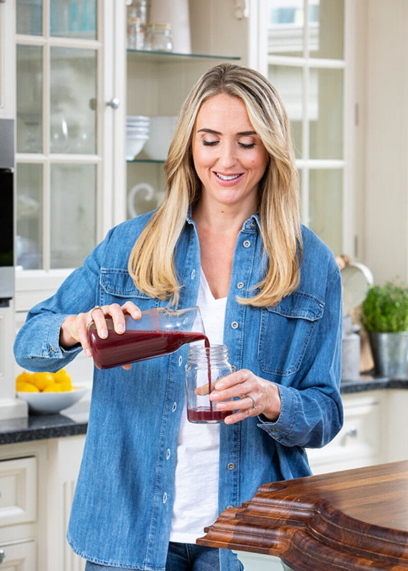 Charlotte Grand, menopause nutritionist, smiling while pouring a smoothie in her kitchen as part of The Menopause Kitchen brand.