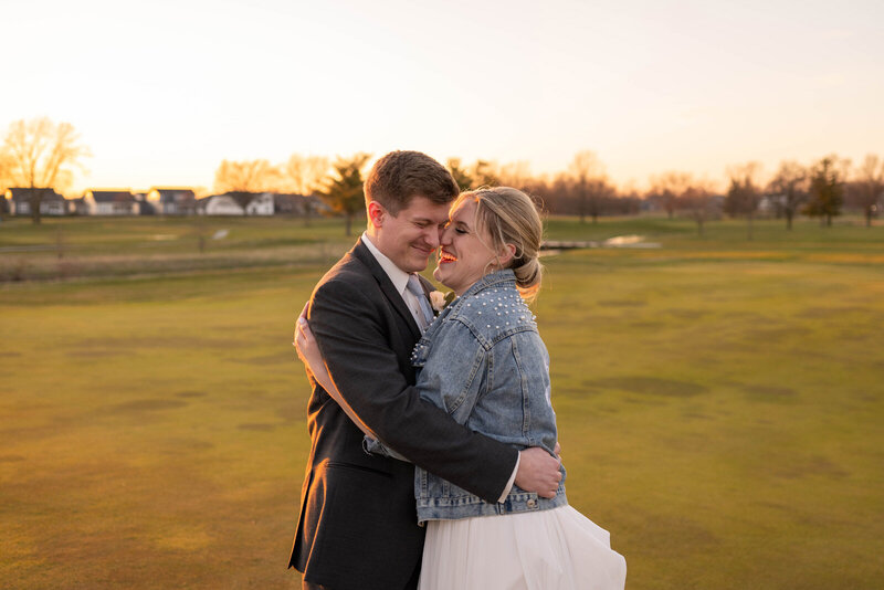 Bride and groom laughing in an open grassy area at sunset.