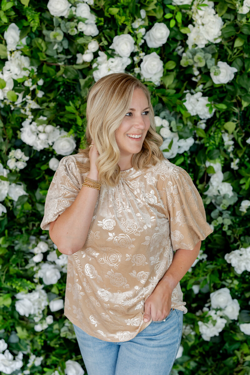 Woman looking to the side standing in front of green and white floral wall.