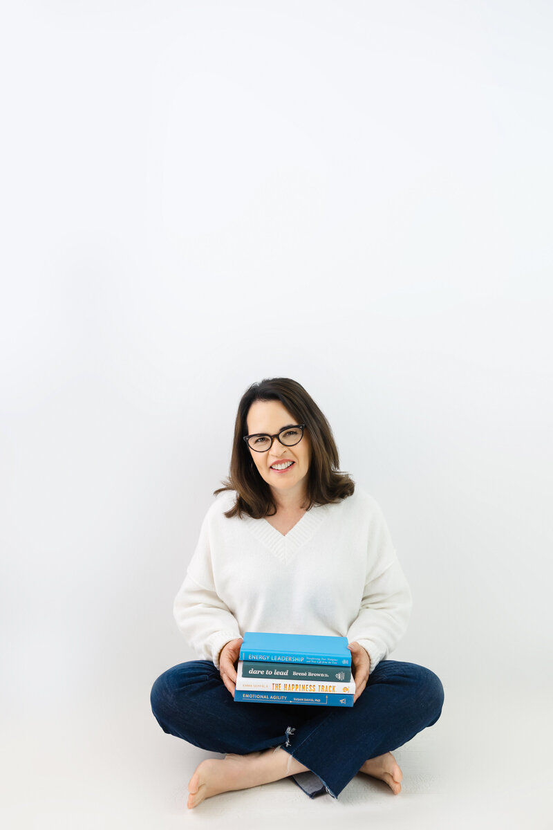Coach sitting cross legged smiling with leadership books promoting emotional resilience
