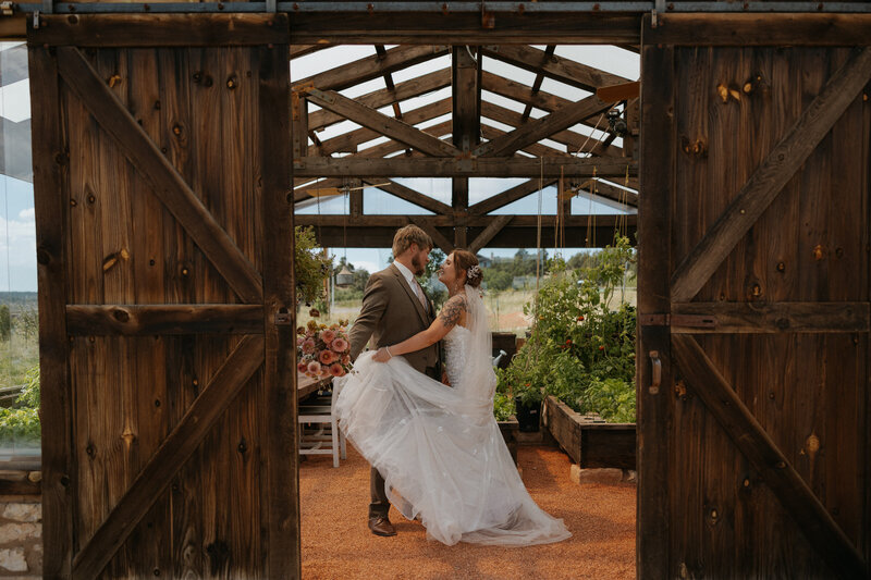 A couple standing close as one holds out the end of their wedding dress 