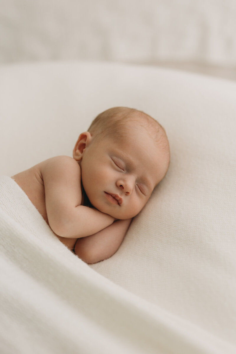 Newborn baby picture taken in Kelowna BC with baby wearing a white bow and wrapped in a white blanket