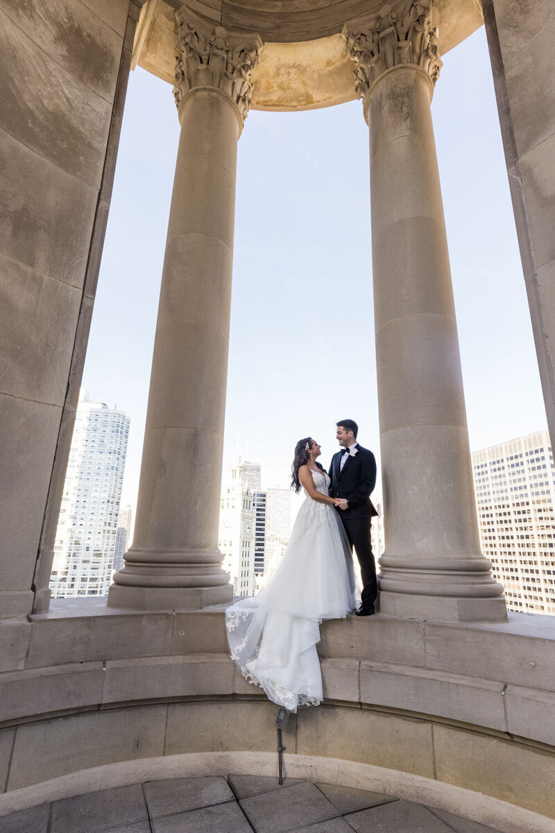 A bride and groom are posing for a picture in front of columns