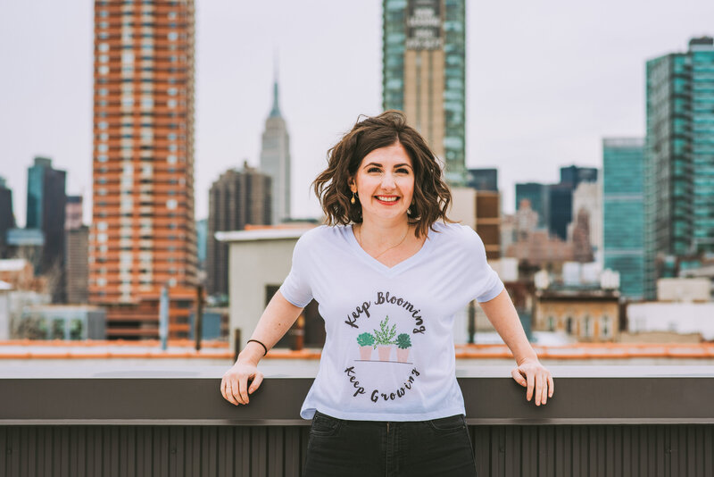 Maria, host of Bloom & Grow Radio podcast, smiles and stand on her roof top in front of NYC skyline