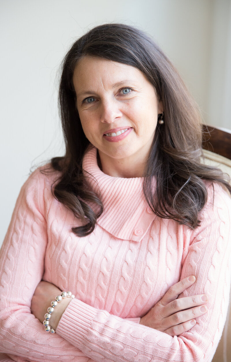 Rachel Sanford in pink sweater seated with arms folded smiling