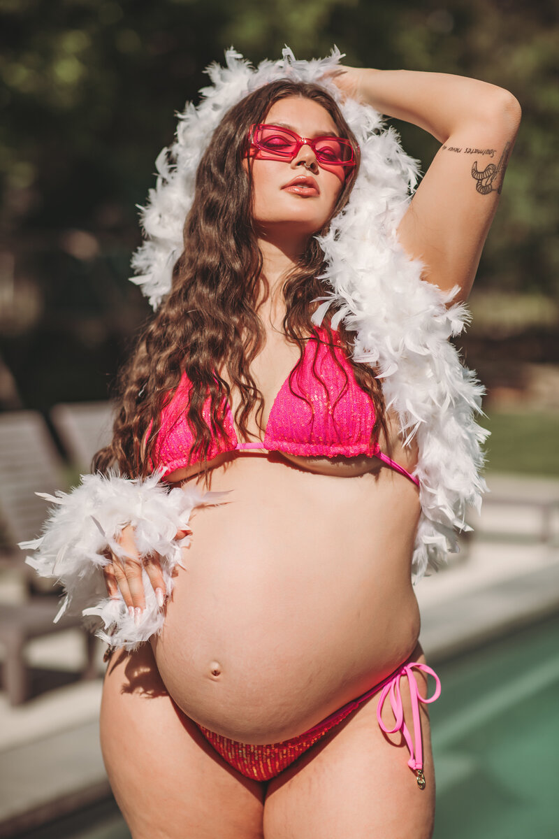 Playful pregnant mother in a hot pink bikini with a feathered boa. 