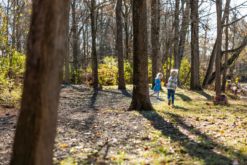 Portrait of siblings playing in the woods and holding giant orange leaves during a family portrait session in Farmington, Missouri. 