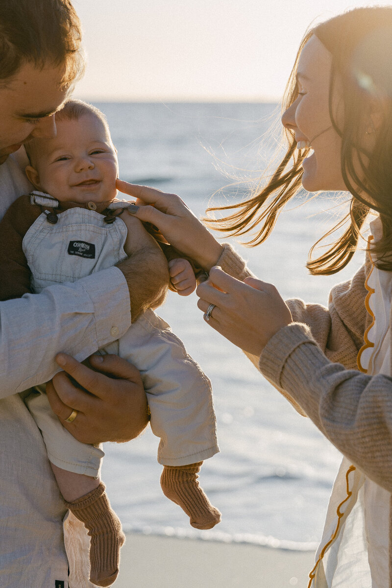 Outdoor beach family photoshoot. Mother and father holding their baby by the water.