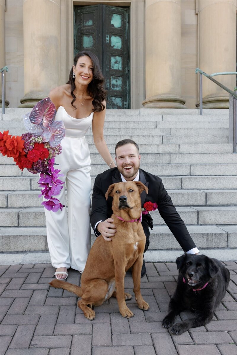 bride and groom posing in at the bottom of the steps in front of the Line Hotel DC with their two dogs and smiling at the camera