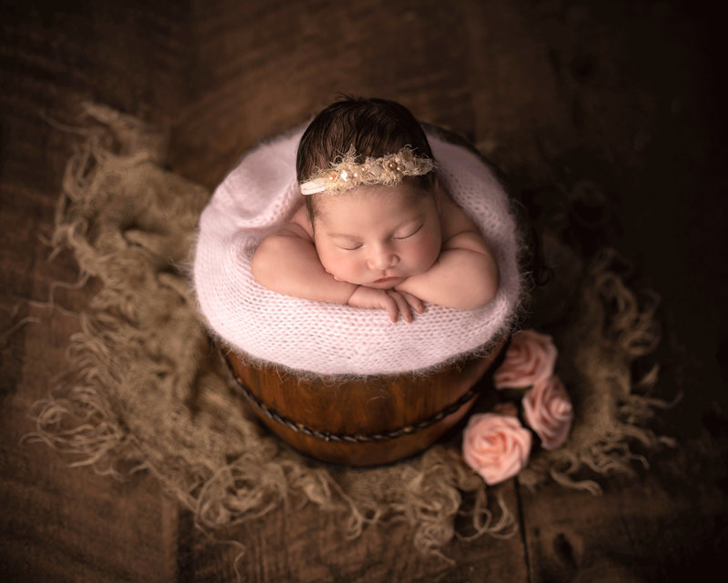 Newborn baby peacefully sleeping in a rustic bucket, wrapped in soft fabric, captured in a charming fine art photography session in Ottawa."