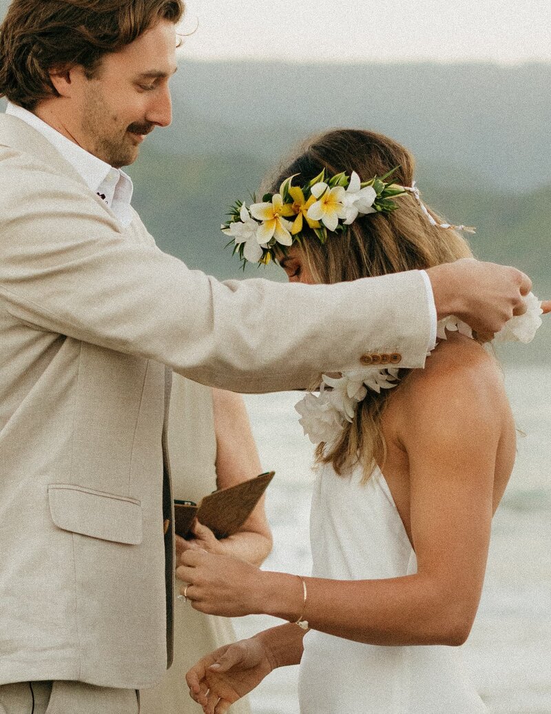 groom giving bride a lei on beach in hawaii
