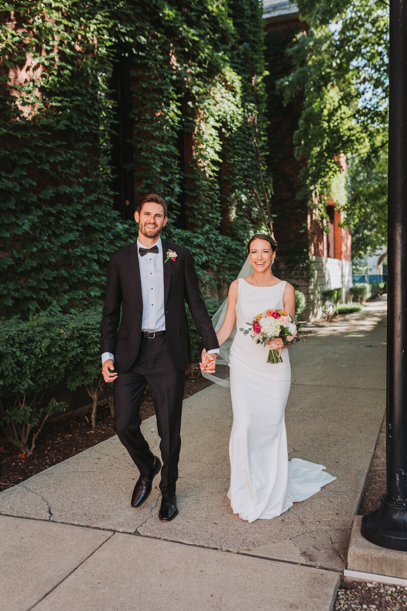 Bride and groom walking next to each other near an ivy wall
