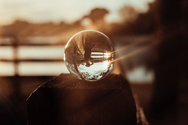 Reflection of a woman posed in a cowgirl hat on a fence  in a glass ball at sunset