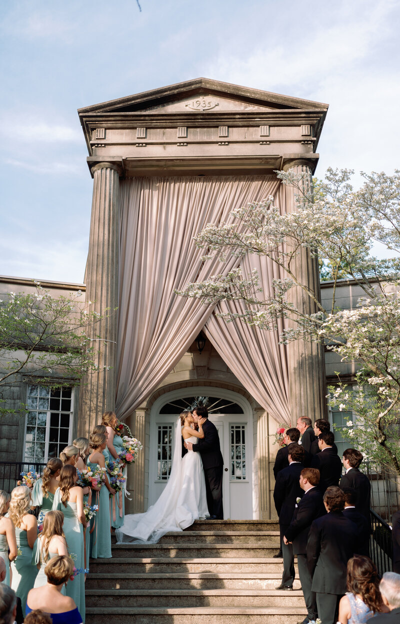 Bride and groom share a kiss at the top of the stone steps during their ceremony exit at Burritt on the Mountain in Huntsville, Alabama, captured by wedding photographer Perry Hancock.