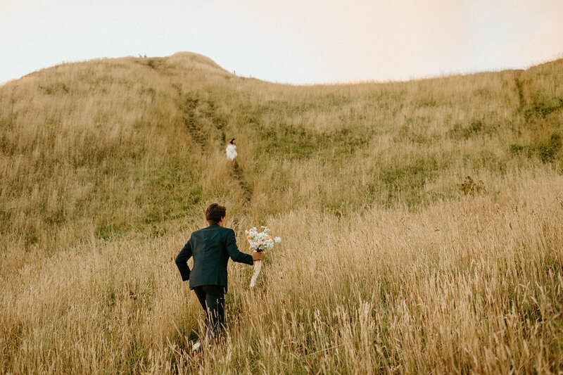 groom running through grassy field toward bride