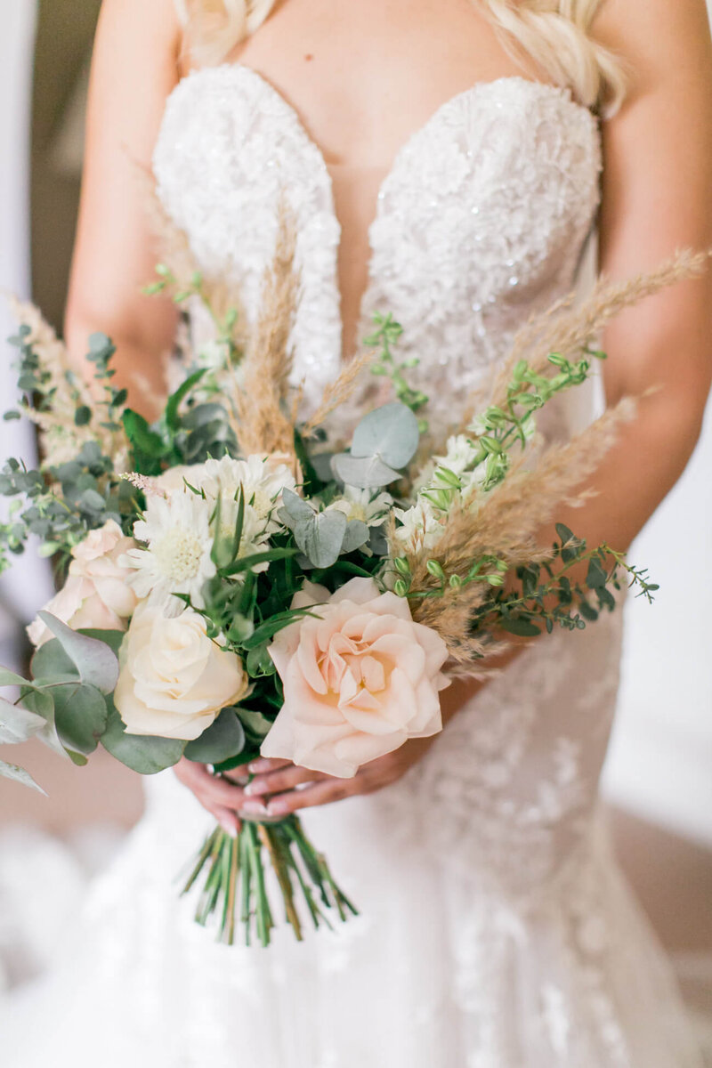 A wedding bouquet with roses and pampas grass being held by a bride