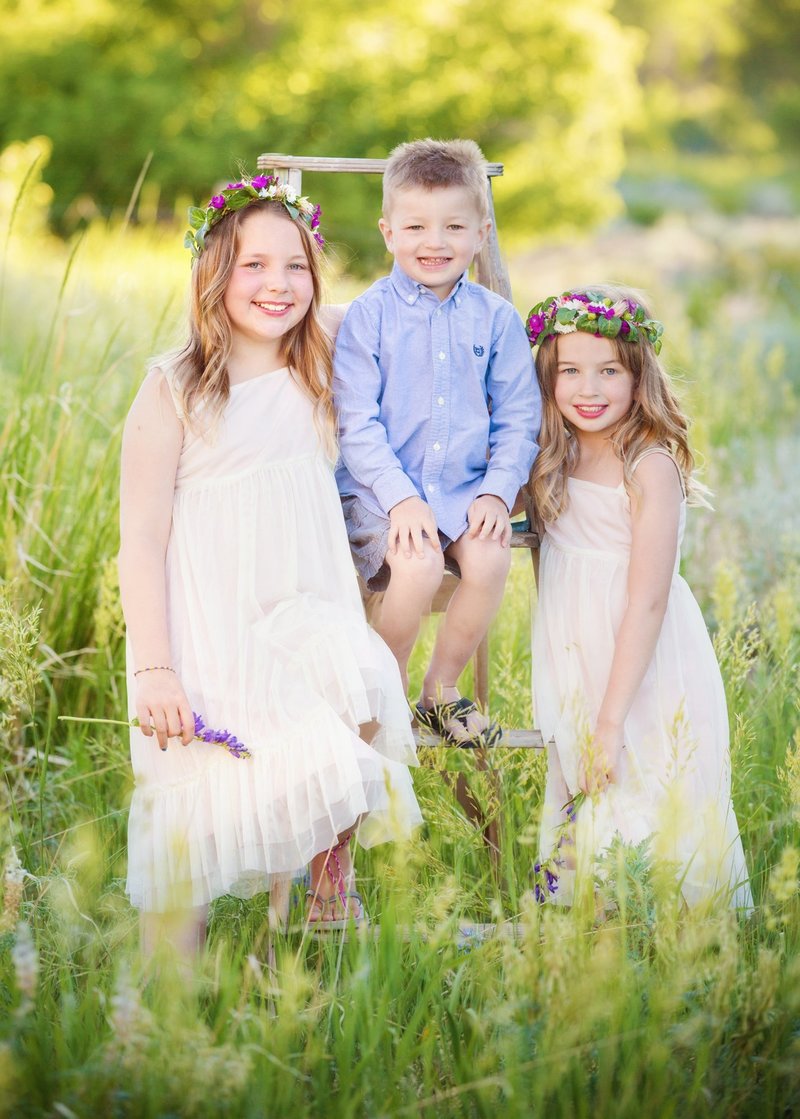 Three brothers and sisters on an antique ladder wearing long ivory dresses with flower crowns in Wyoming.