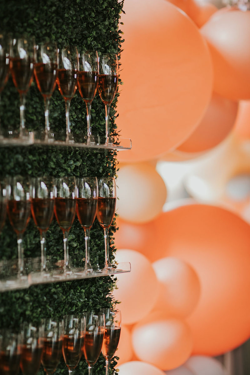 Champagne wall with rose champagne with orange and peach balloons on a boxwood wall