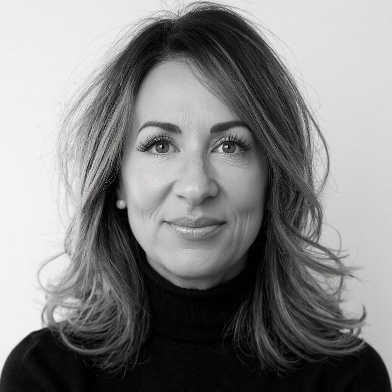 CEO of Sweet Pea Ink Creative with wavy brown hair wearing a white short-sleeve button-up shirt and beige pants stands indoors with hands in pockets, embodying the relaxed confidence of a brand strategist at Sweet Pea Ink Creative.