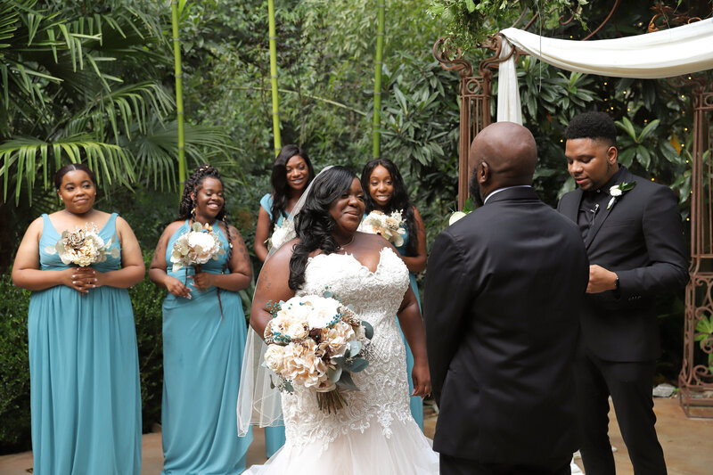 Black Couple getting married under a decorated arch with bridesmaids wearing blue at the River Road and Jasmine House in South Carolina