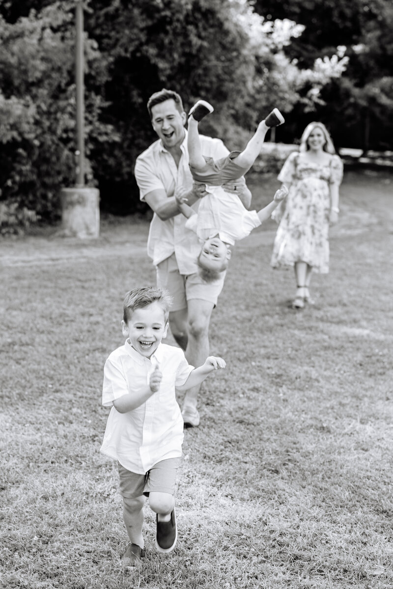 Black and white photo of family of four running through the grass