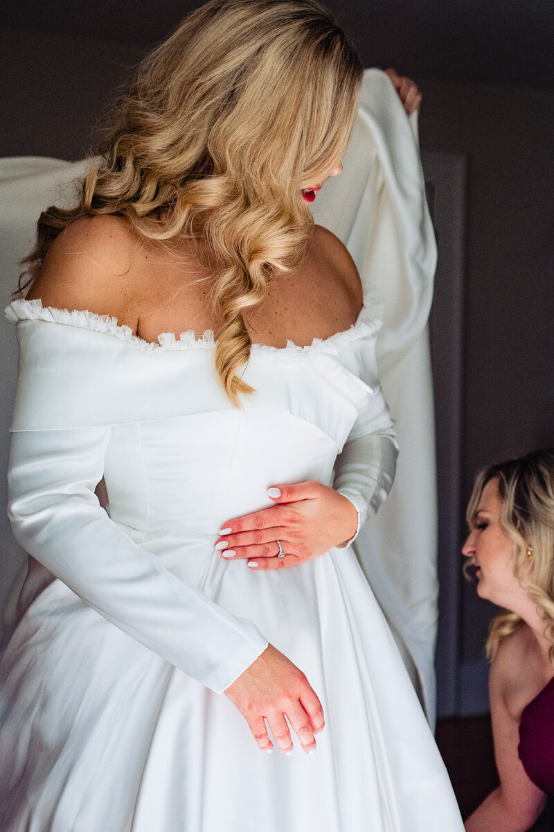 A bride gets her dress on as her blonde hair covers her face except for her red lipstick