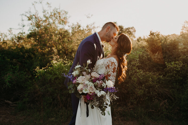 bride and groom kiss while bride holds bouquet outside