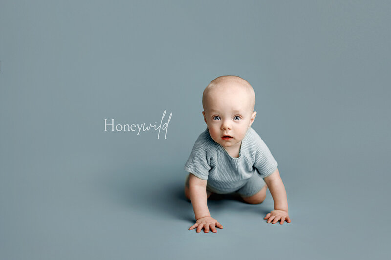Baby girl with blue eyes wearing a floral dress and white bow, sitting in a white box with a soft balloon backdrop during a professional portrait session in Grand Rapids, Michigan