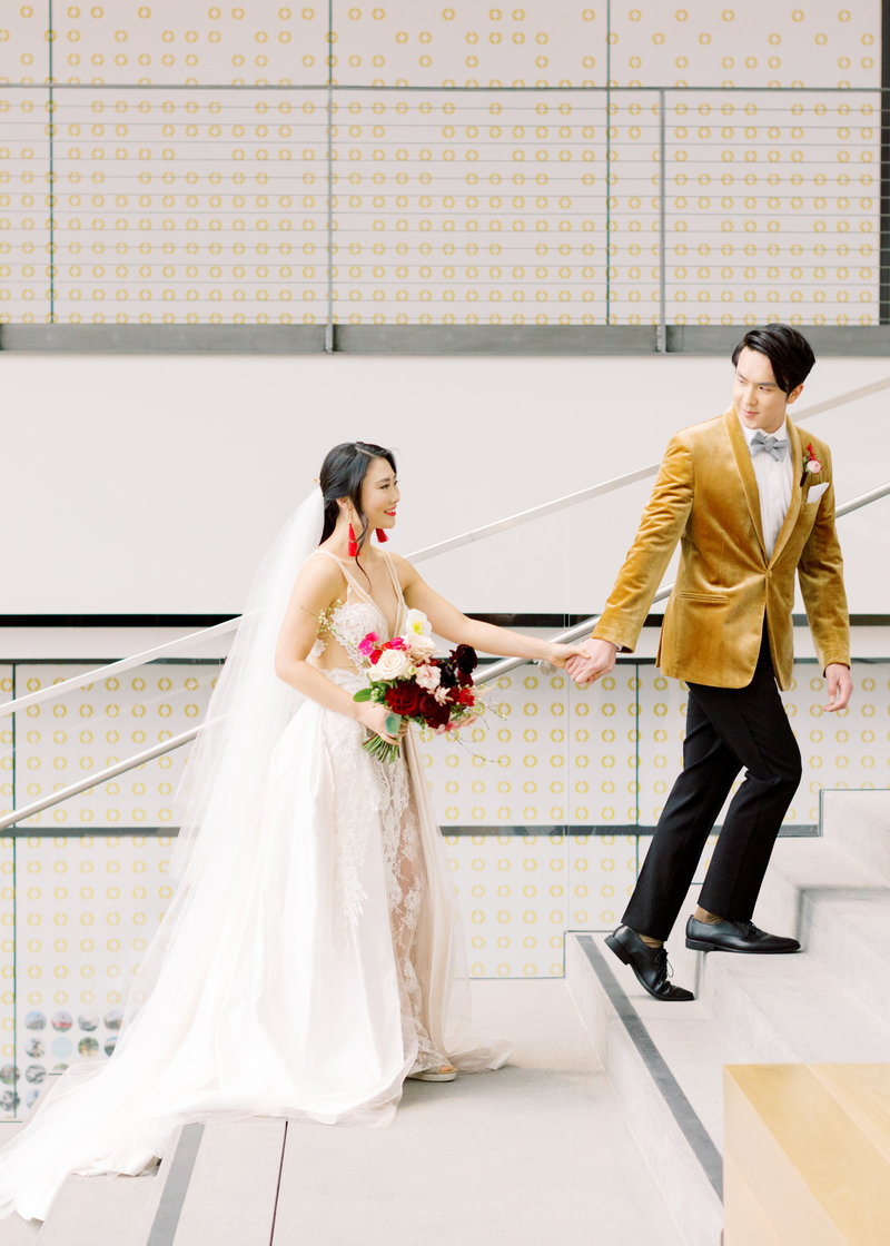 A sophisticated bride and groom ascend a grand staircase, captured in a luxury editorial wedding photography style.