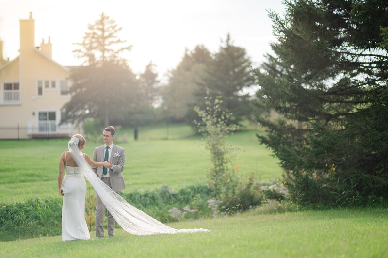 La mariée regarde tendrement son mari tandis que son long voile s’étend derrière elle, scène romantique et lumineuse à l’Auberge West Brome en Montérégie, lors d’un mariage empreint de douceur et de charme naturel