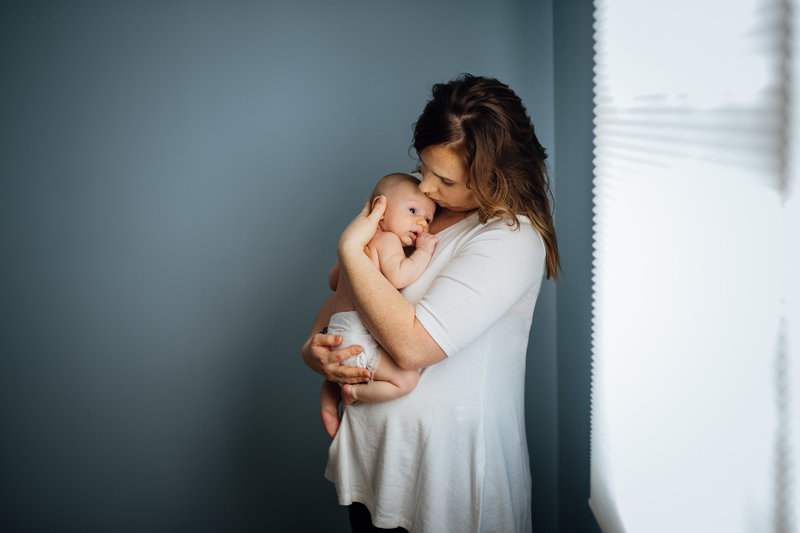 mom holding newborn baby in front of blue wall