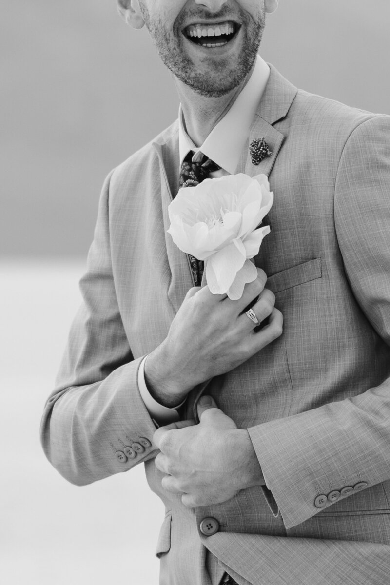 A man is laughing as he pins a flower to his suit jacket
