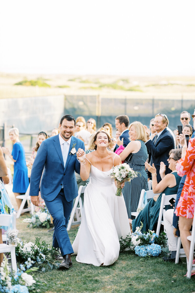 couples recesses down the aisle lined with blue hydrangea as guests cheer at Cape Cod wedding by Lynne Reznick Photography