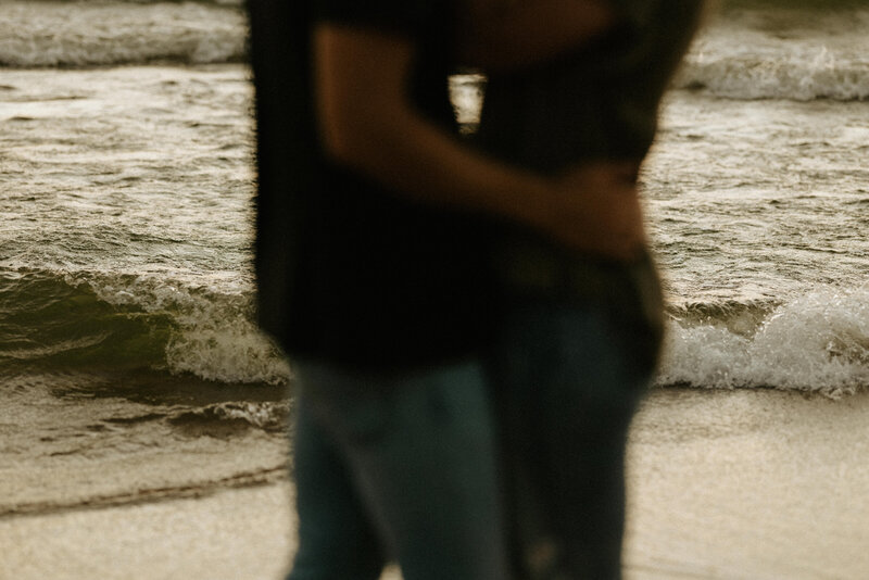 A close up photo of a couple's hips while they hug in front of Lake Michigan