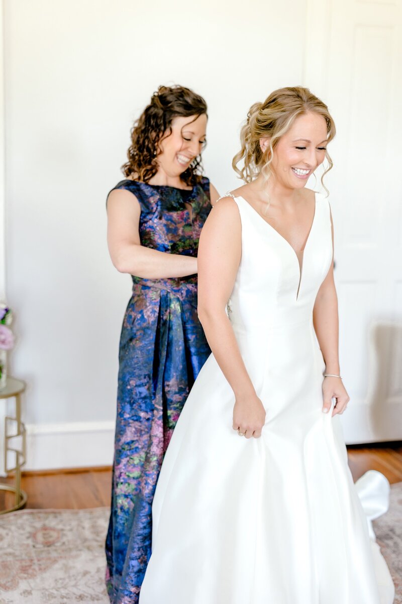 A bridesmaid assists the bride with her gown, capturing a heartfelt moment of preparation before the ceremony, organized by Socially Significant Events.