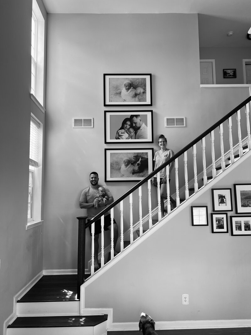Mom holding newborn baby posing with a photo album and wall art