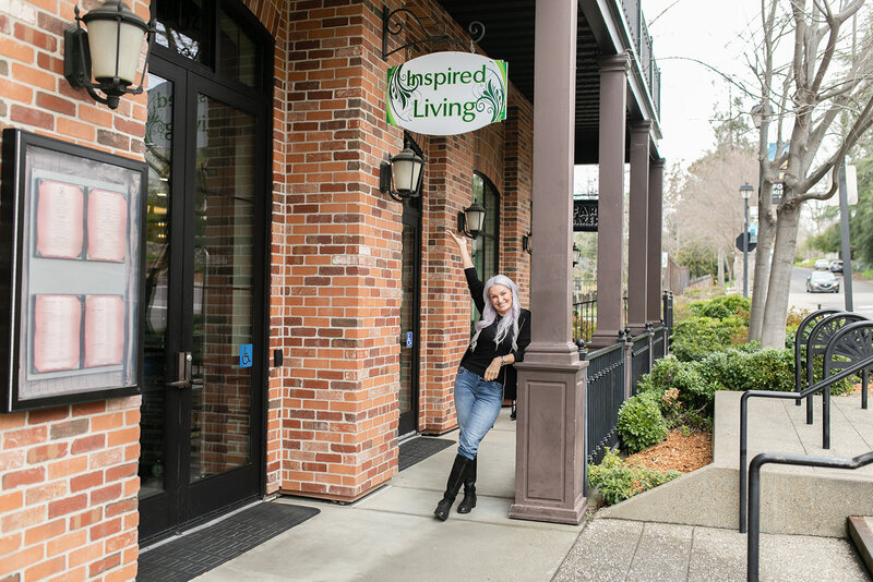 Dawna Weiss smiling and pointing to the Inspired Living sign outside her wellness office in Folsom, California