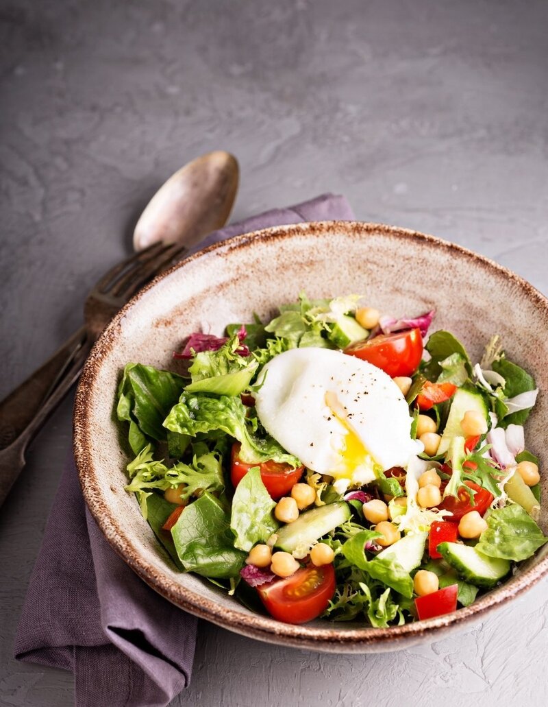 Fertility-friendly salad with mixed greens, chickpeas, tomatoes, cucumber, and a poached egg – ideal for a nutrient-rich fertility diet when trying to conceive.