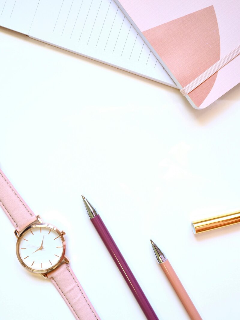 Flat lay with pink leather watch, colorful pens, and notebook for professional coaching and career planning