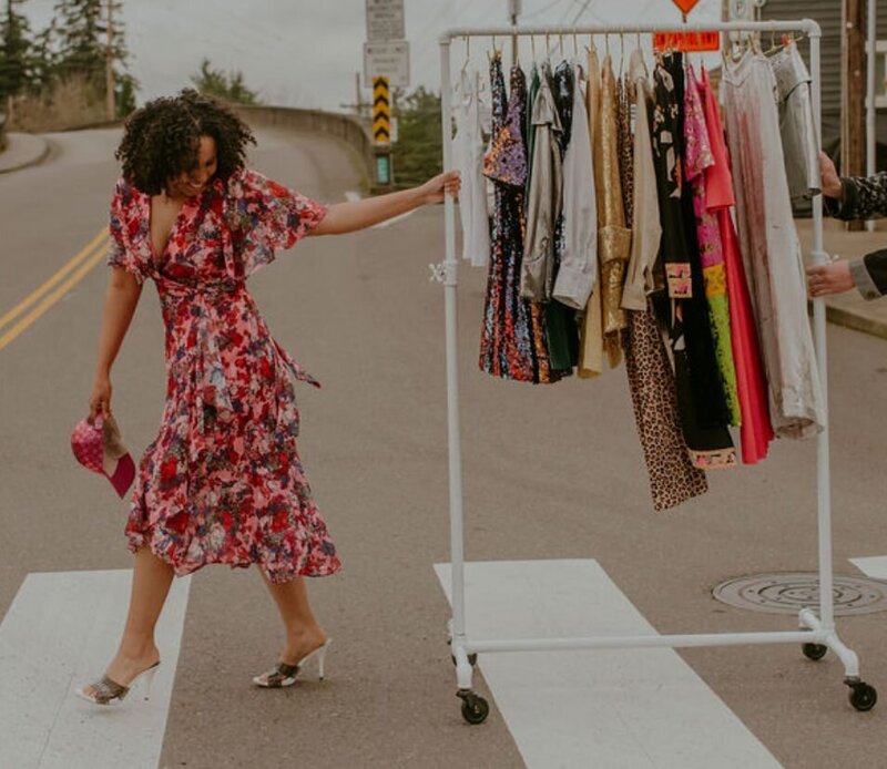 A person pulling a clothing rack across a sidewalk 