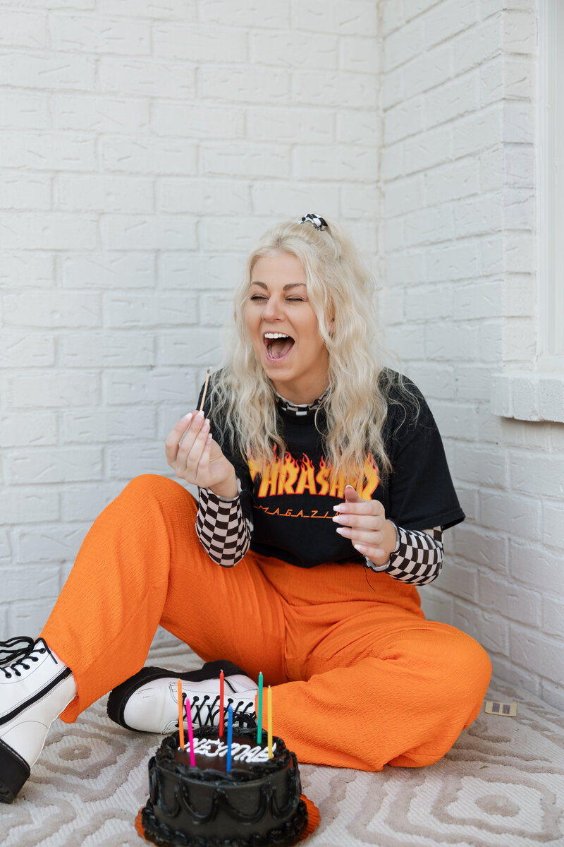 Sophie sitting on the ground with a black birthday cake in front of a white background laughing