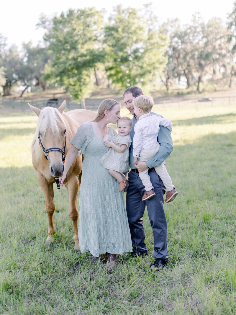 Family portrait of mom, dad, 4 year old boy, 1 year old girl and palomino horse on a horse farm in soft afternoon golden light by NH family photographer Fieldstone Studio.
