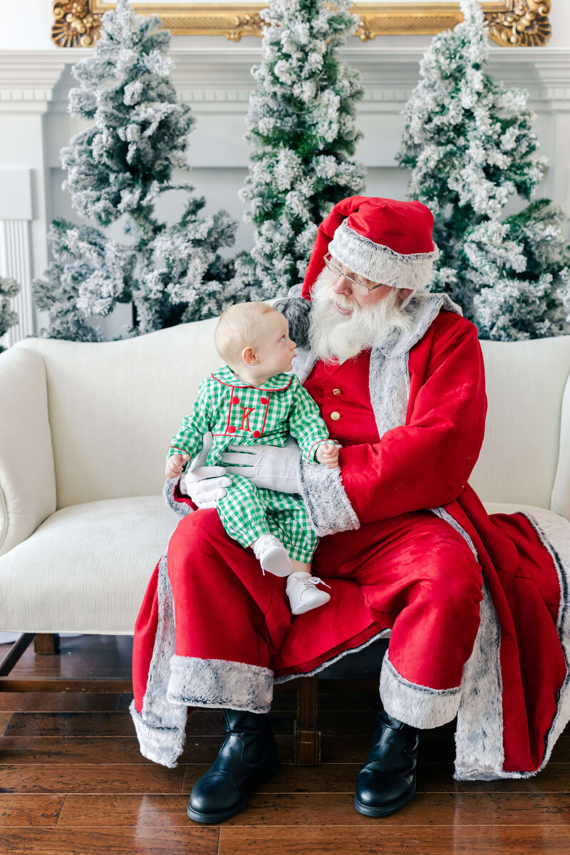 Baby looking at santa while sitting on his lap at santa mini sessions
