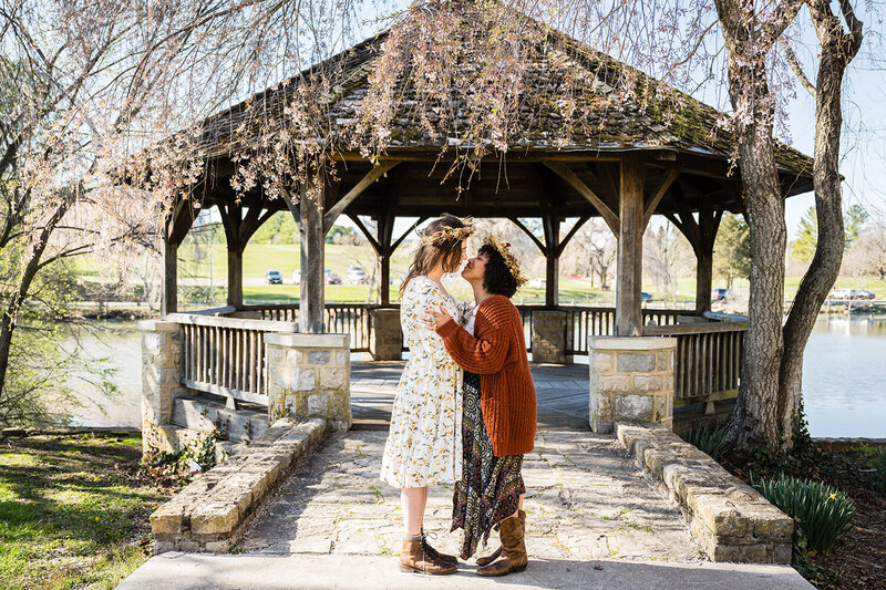 An LGBTQ+ couple goes in for their first kiss in front of the gazebo at Duck Pond on Virginia Tech's campus in Blacksburg. They are photographed on an early spring day by their Virginia elopement photographer.