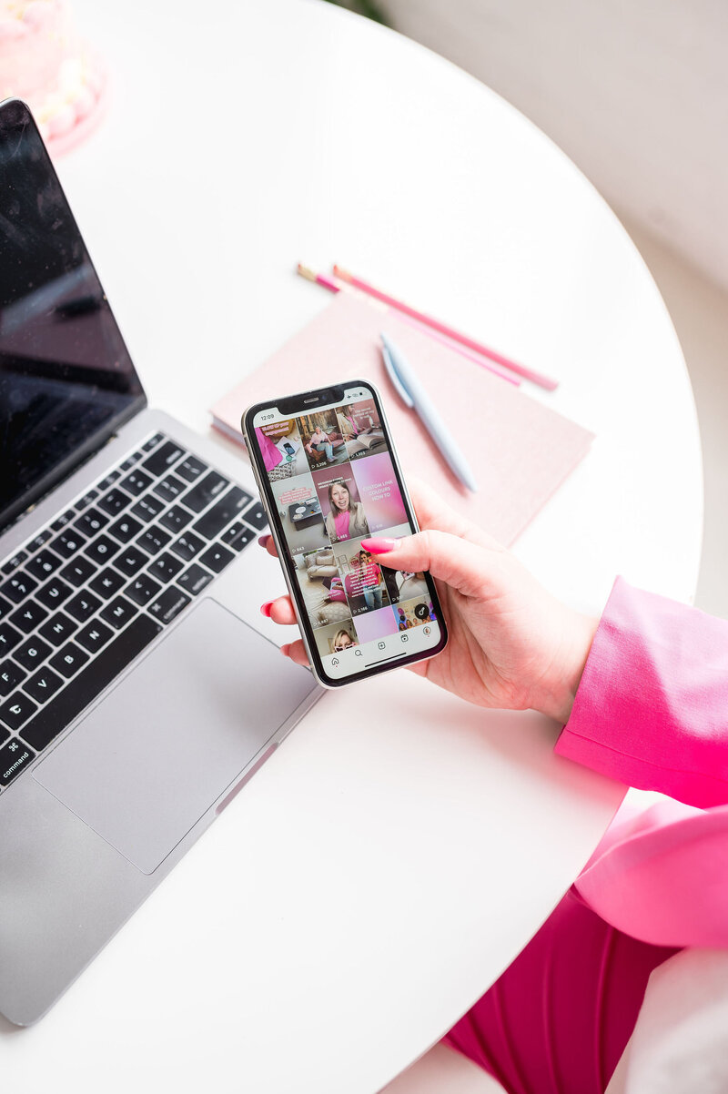 Hand with a pink sleeve holding up a phone with an Instagram grid on the screen