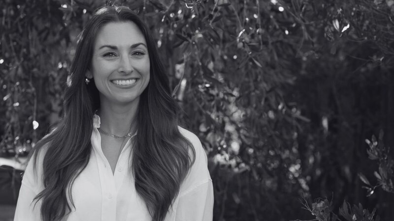 A photo of Tara Accardo, with long brown hair who is smiling in a white button up shirt, from Losses Become Gains