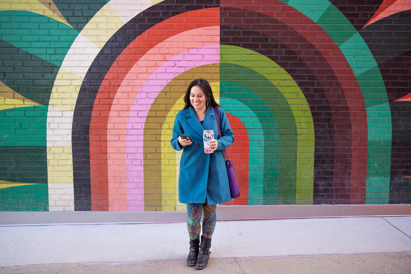 A-creative-entrepreneur-poses-with-her-phone-in-front-of-painted-baltimore-murals-for-her-branding-lifestyle-headshots